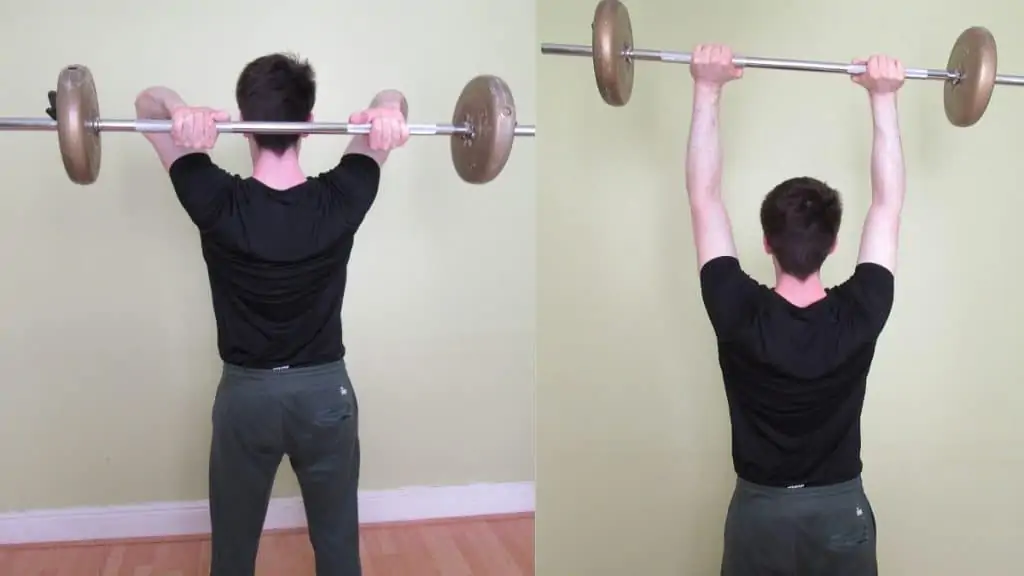 A man doing a standing overhead tricep extension with a barbell