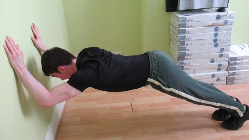 A man doing a tricep extension against a wall at home