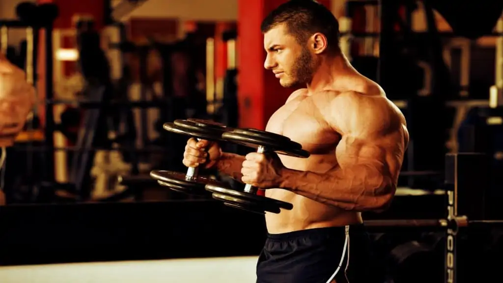 A bodybuilder in the gym working his biceps with a 45 lb dumbbell curl