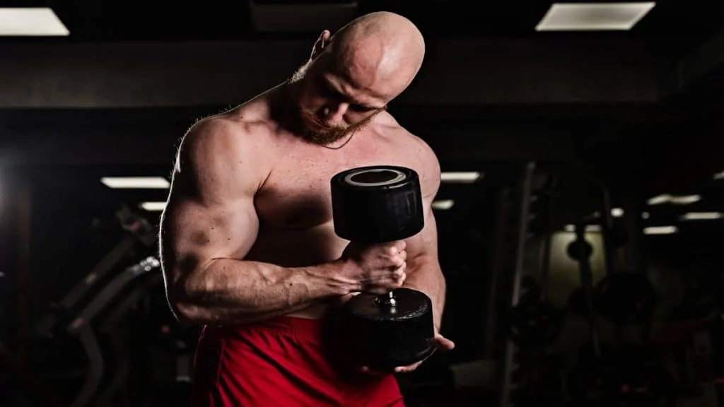 A muscular man performing a 60 lb bicep curl with a dumbbell