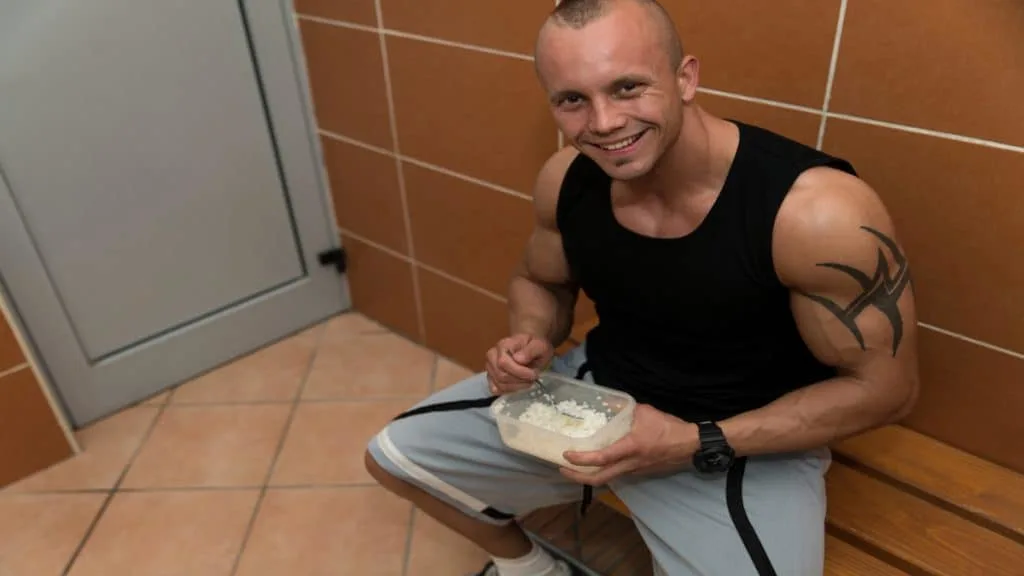 A bodybuilder at the gym eating out of tupperware