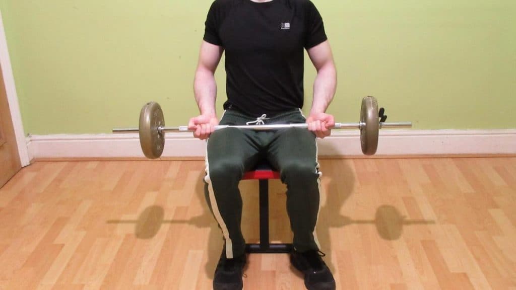 A man performing a sitting barbell curl for his biceps