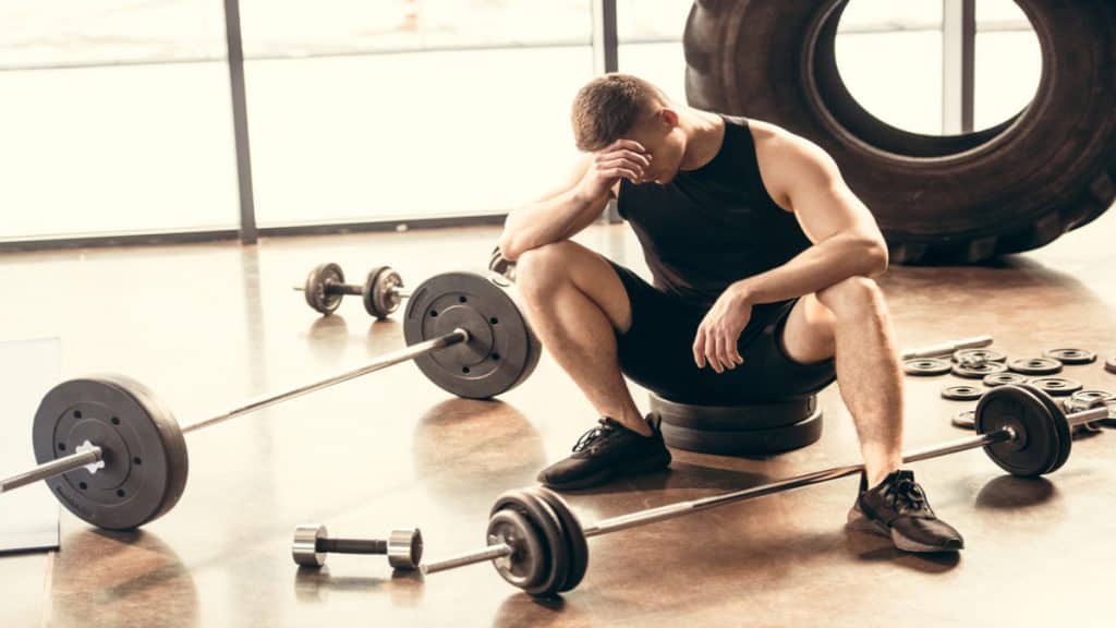 An upset man sitting next to some weights
