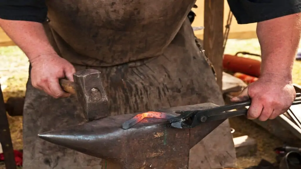 A blacksmith with thick forearms holding a hammer