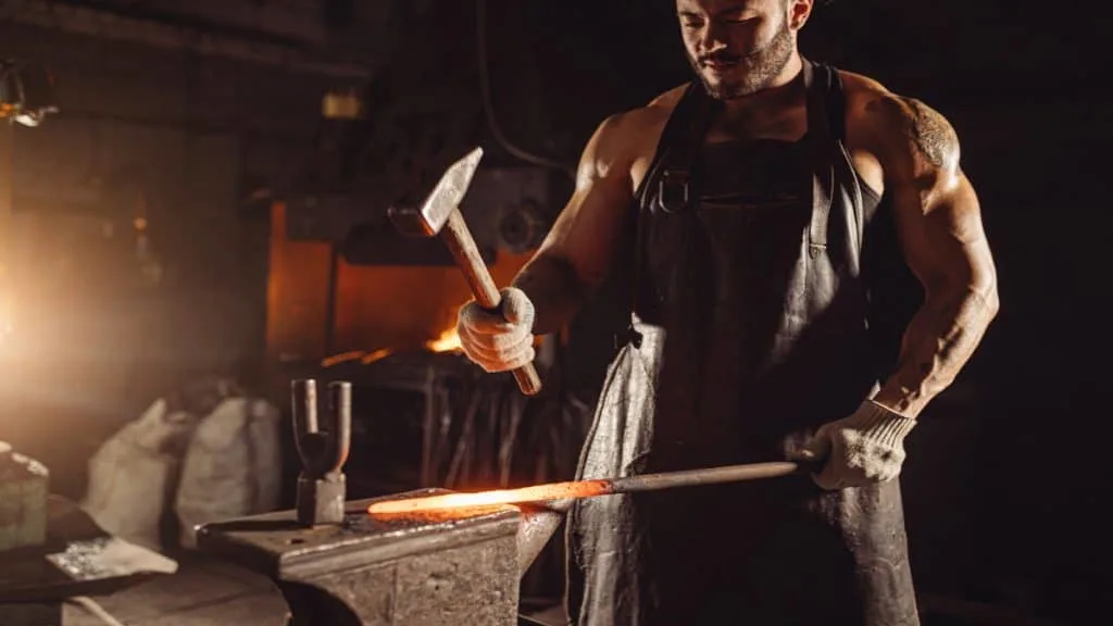 A blacksmith with muscular forearms holding a hammer