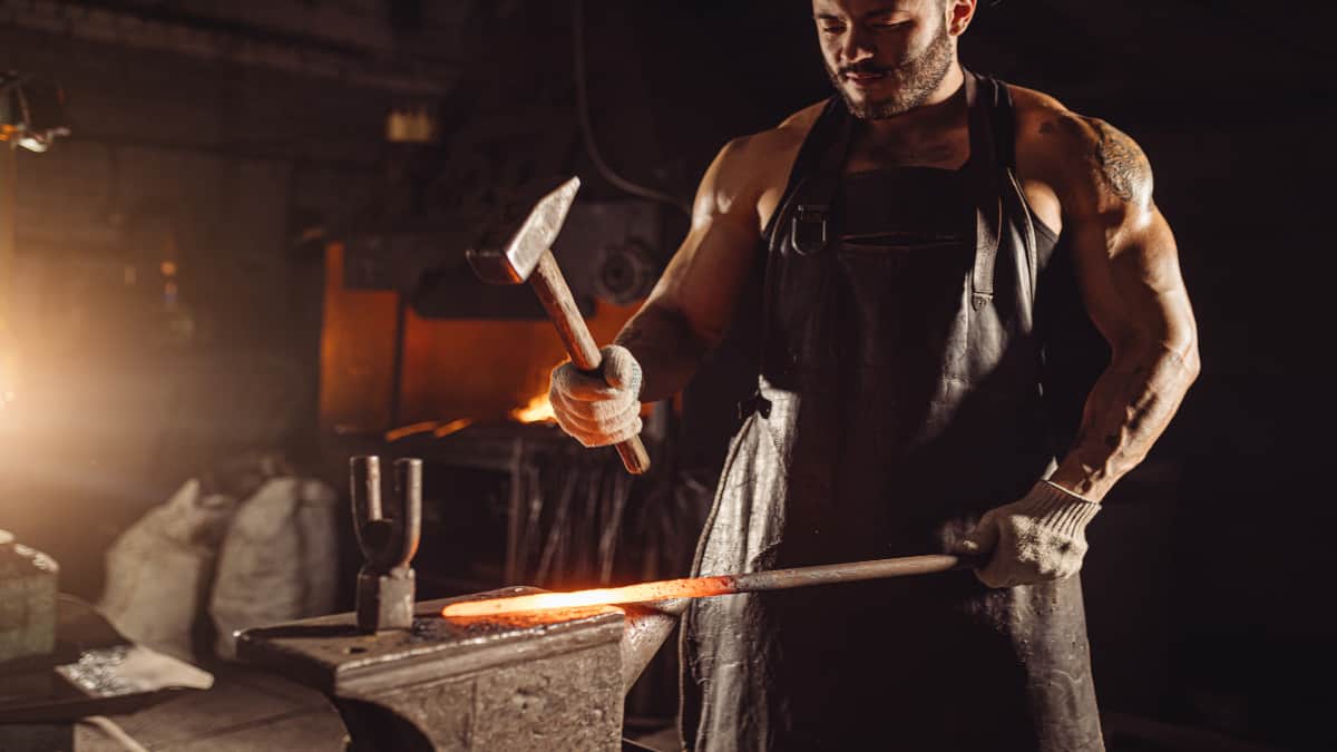 A blacksmith with muscular forearms holding a hammer