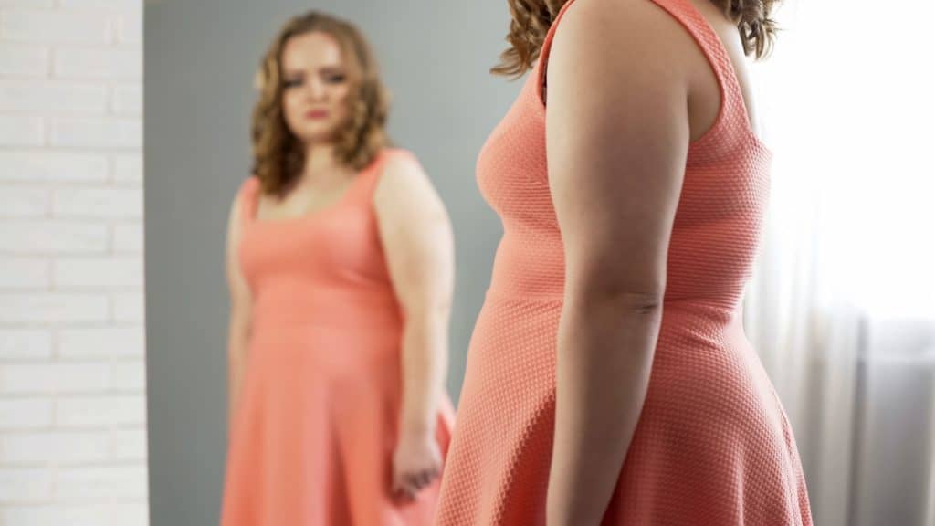 A woman looking at her forearm fat in the mirror