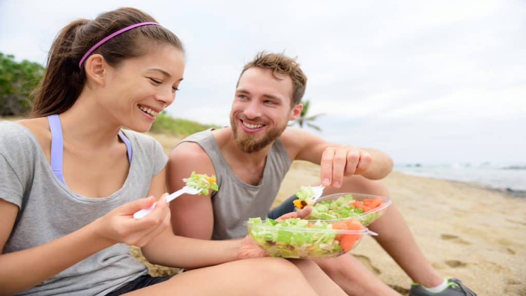 A man and a woman eating salad at the beach