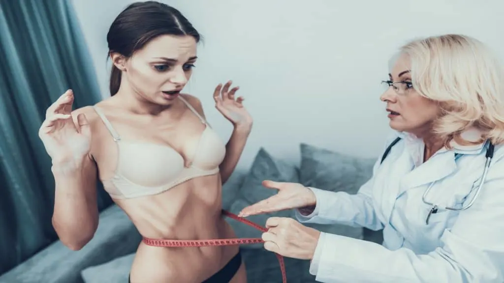 A skinny woman getting her 14 inch waistline measured by a doctor