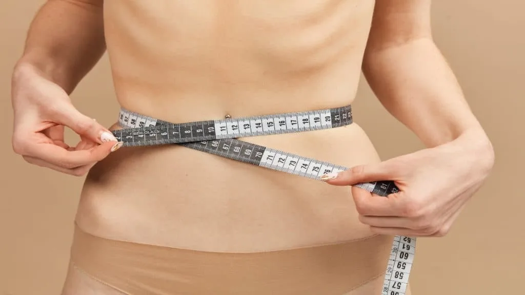 A woman holding a tape around her 17.5 inch waist