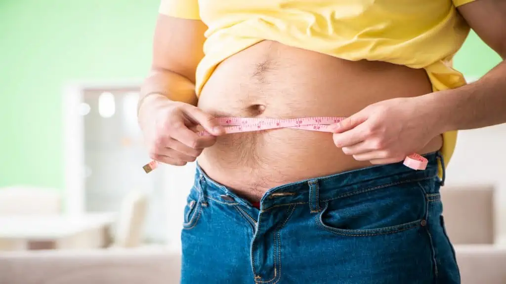 An overweight man holding a tape around his 36 in waist