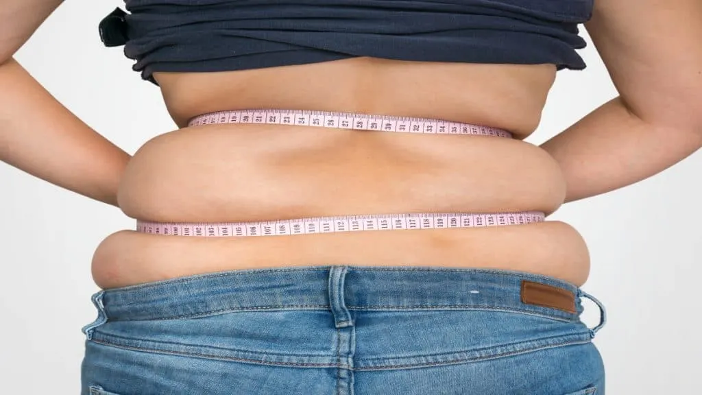 An overweight woman holding a tape around her 42 inch waist