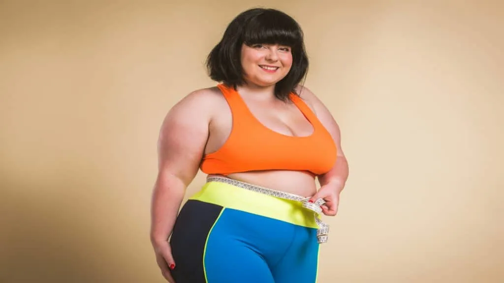 An overweight woman holding a tape around her 44 inch waist