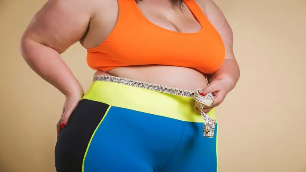 An obese woman measuring her 44 inch waistline