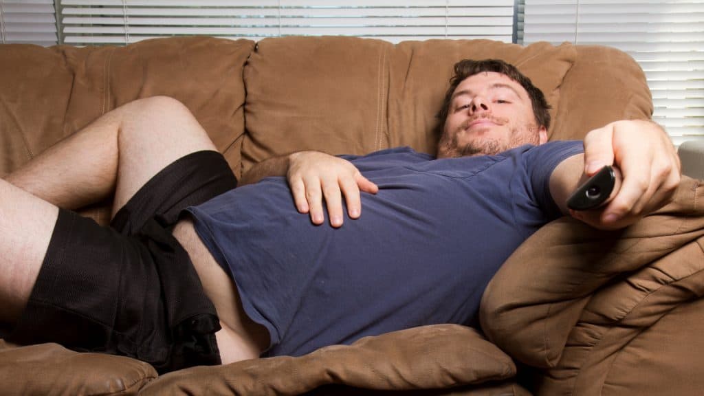 An obese man with a 52 inch waistline sitting on the sofa