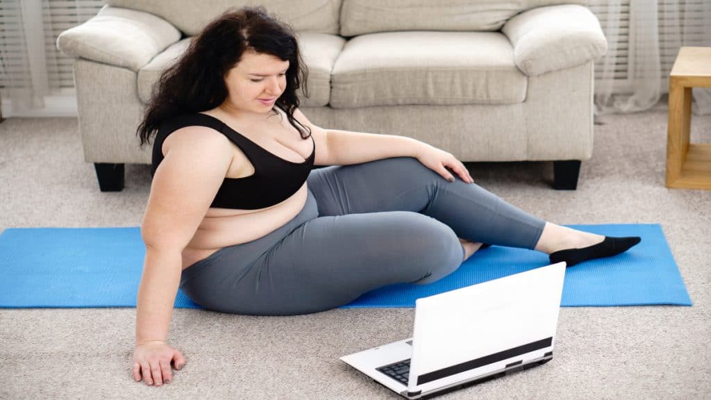 An overweight woman with a 53 in waist working out in her living room