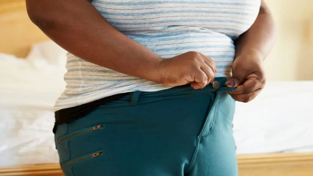 A woman tyring to fasten her 54 in waist pants