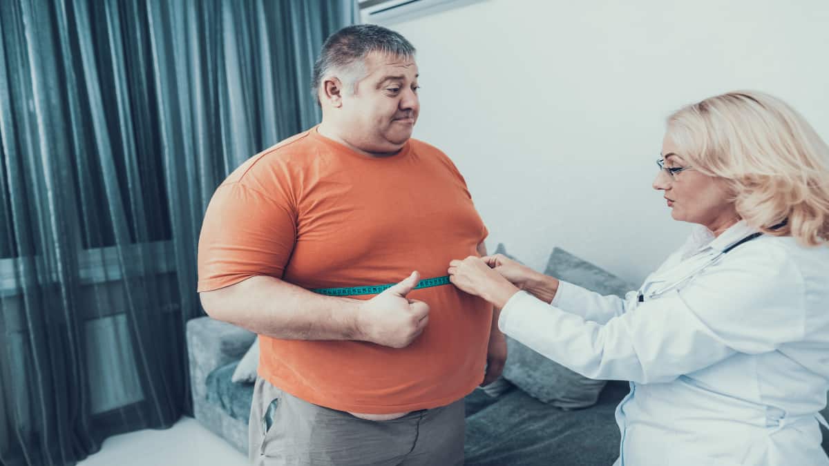 Ab obese man having his big 54 inch waist measured by a doctor