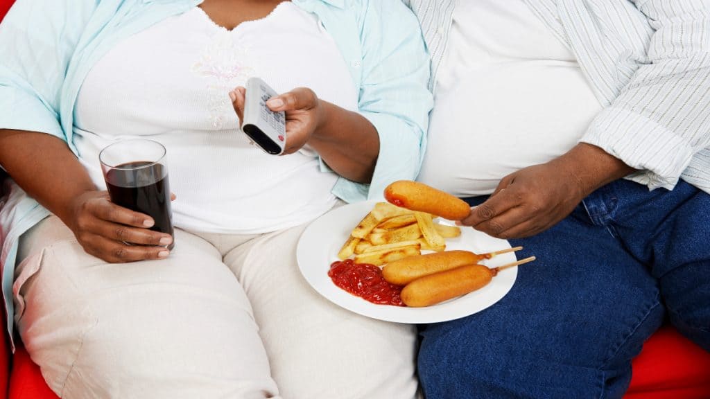 An overweight couple eating food and watching TV
