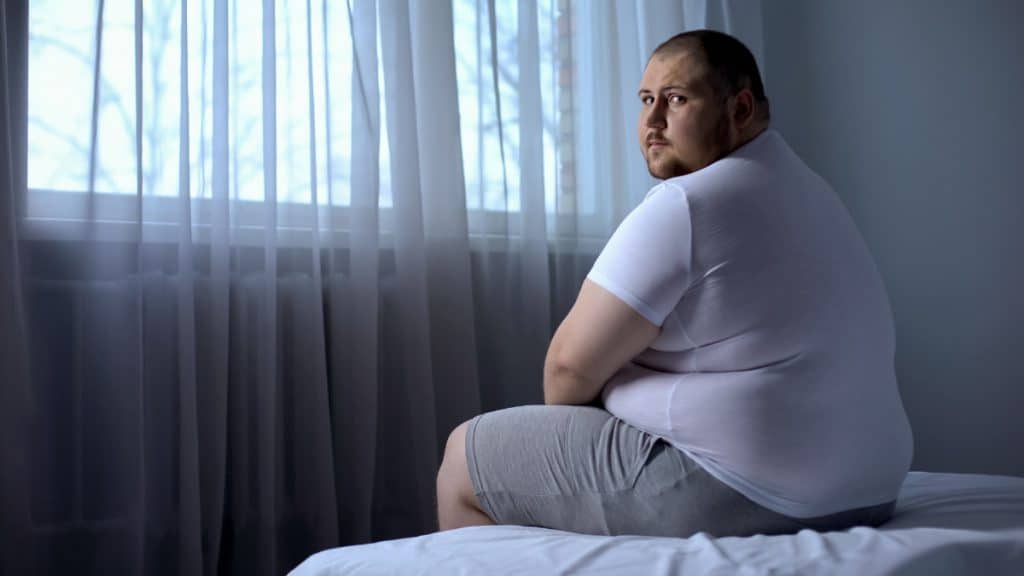 An obese man with a 62 inch waist sat on his bed
