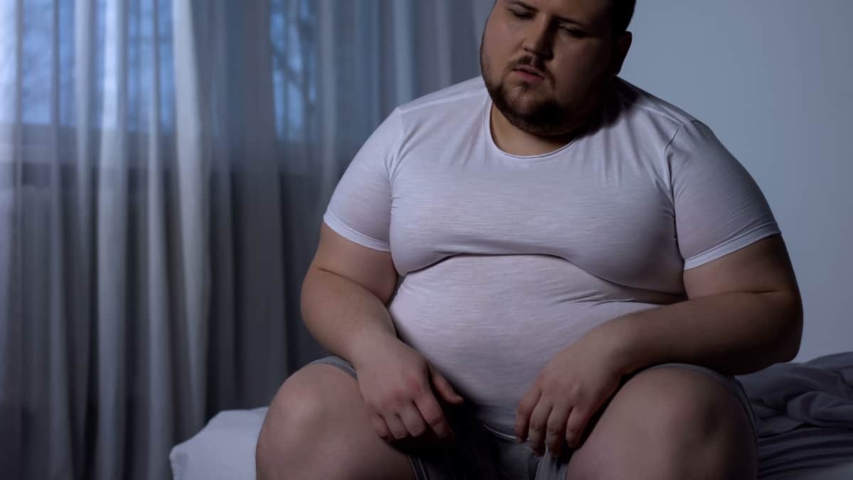 A sad fat man with a 64 inch waist sat on the bed