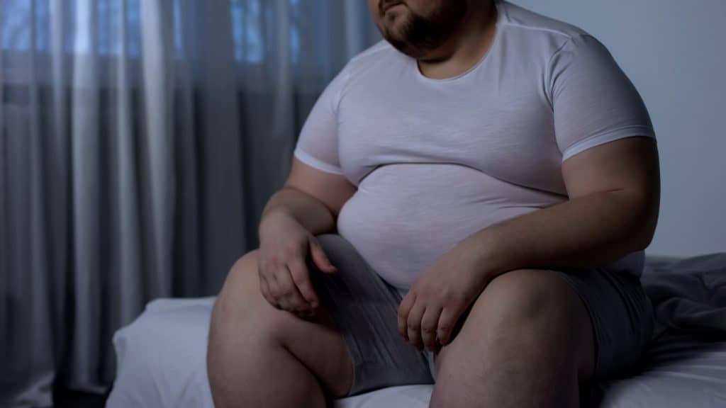 A fat man with a big 65 inch waist sat on the edge of his bed