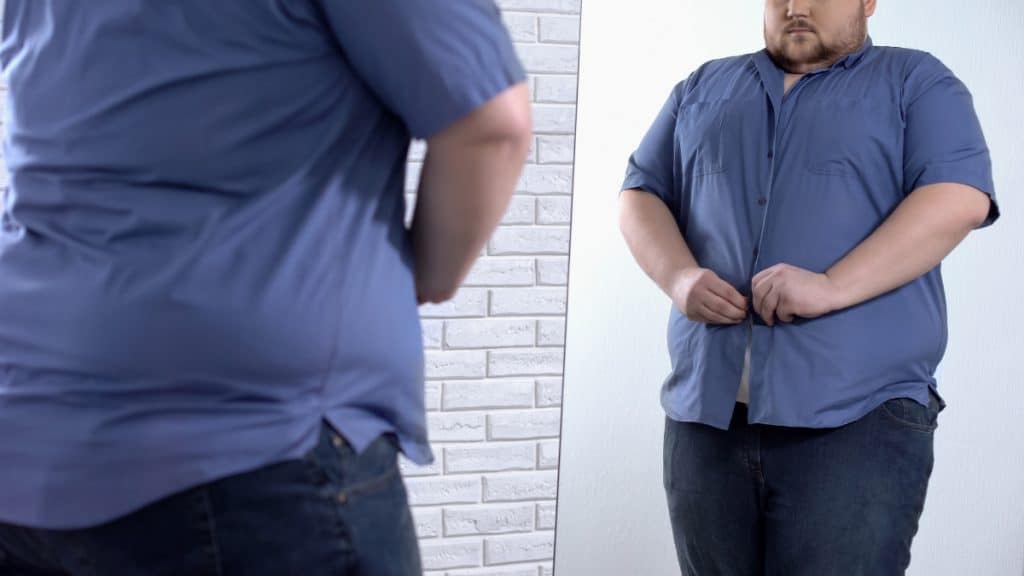 A man trying to fasten his shirt around his 65 inch waistline
