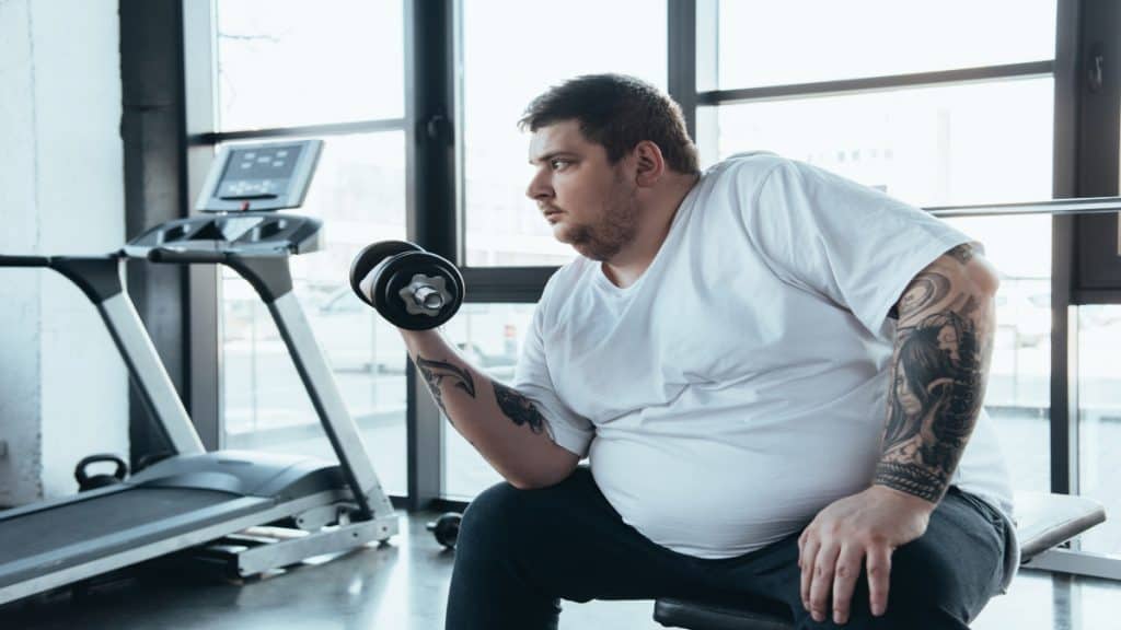An obese man with a 67 inch waist doing some exercises at the gym