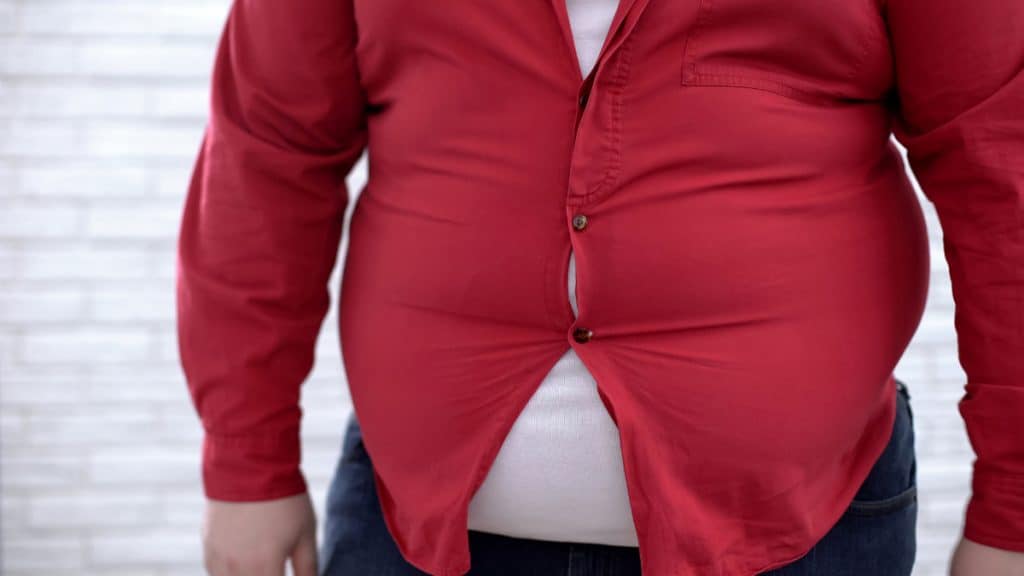 An obese man's big 69 inch waist pushing through his shirt