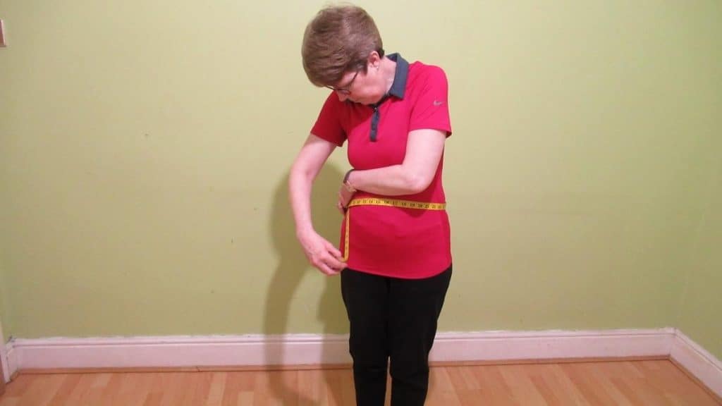 A woman demonstrating how to measure your waist correctly with a tape measure