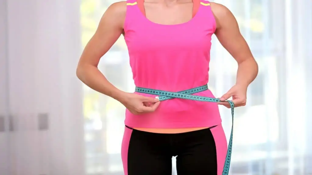 A woman holding a big tape measure around her 27 inch waist