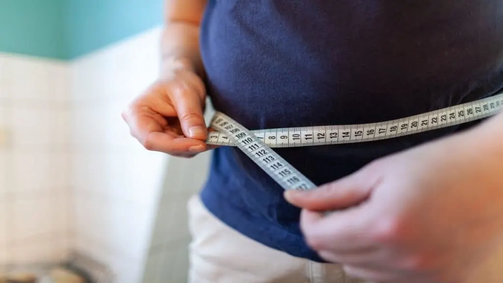 A teenage boy taking his waist measurement