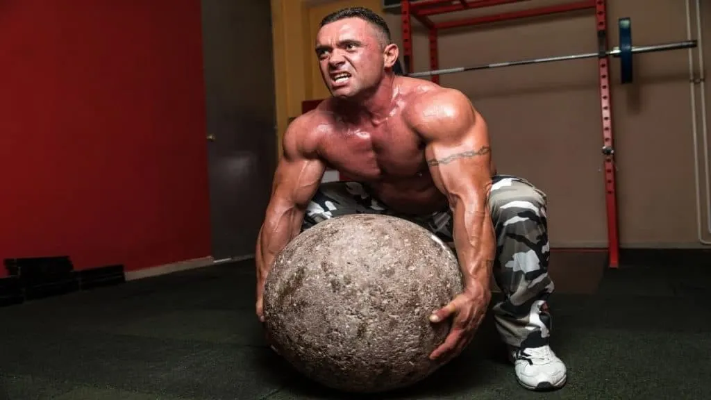 A man with 30 inch shoulders picking up a large stone