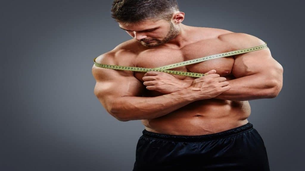 A muscular man measuring his broad 24 inch shoulders