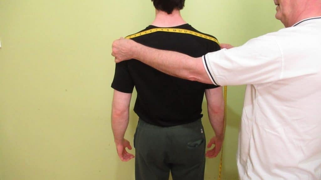 A man showing how to measure your shoulders with a tape measure to determine their width