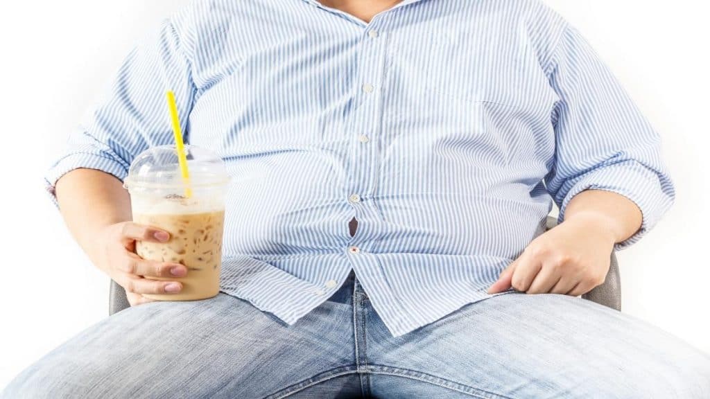 An obese man sat on the sofa with a drink