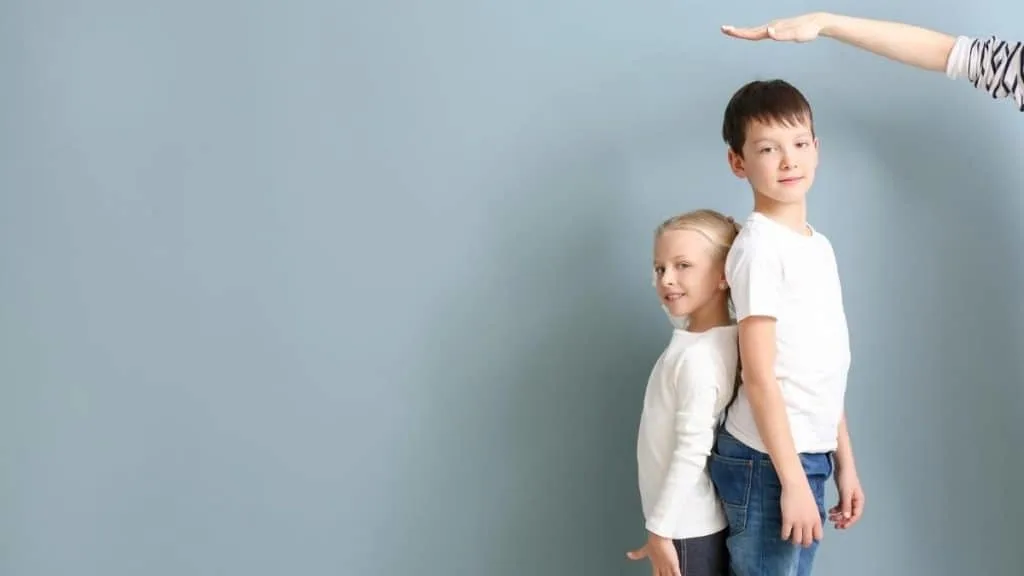 A boy and girl standing back to back in order to measure their heights