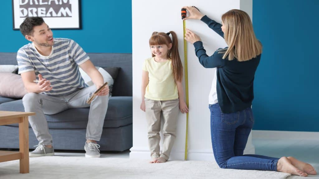 A girl getting her height measured by her parents