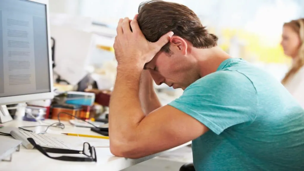 A man sat at his desk looking stressed