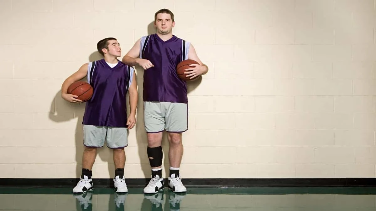 A tall 6'10 man standing next to his friend