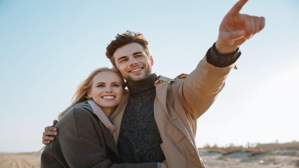 A man pointing with one arm around his girlfriend